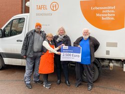 Vier Personen vor Lieferwagen der Bremerhavener Tafel mit einem Spendenscheck.