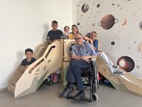 Sensorische Spielecke mit 3 Kindern und 2 Pflegefachkräften sowie dem Chefarzt im Rollstuhl.